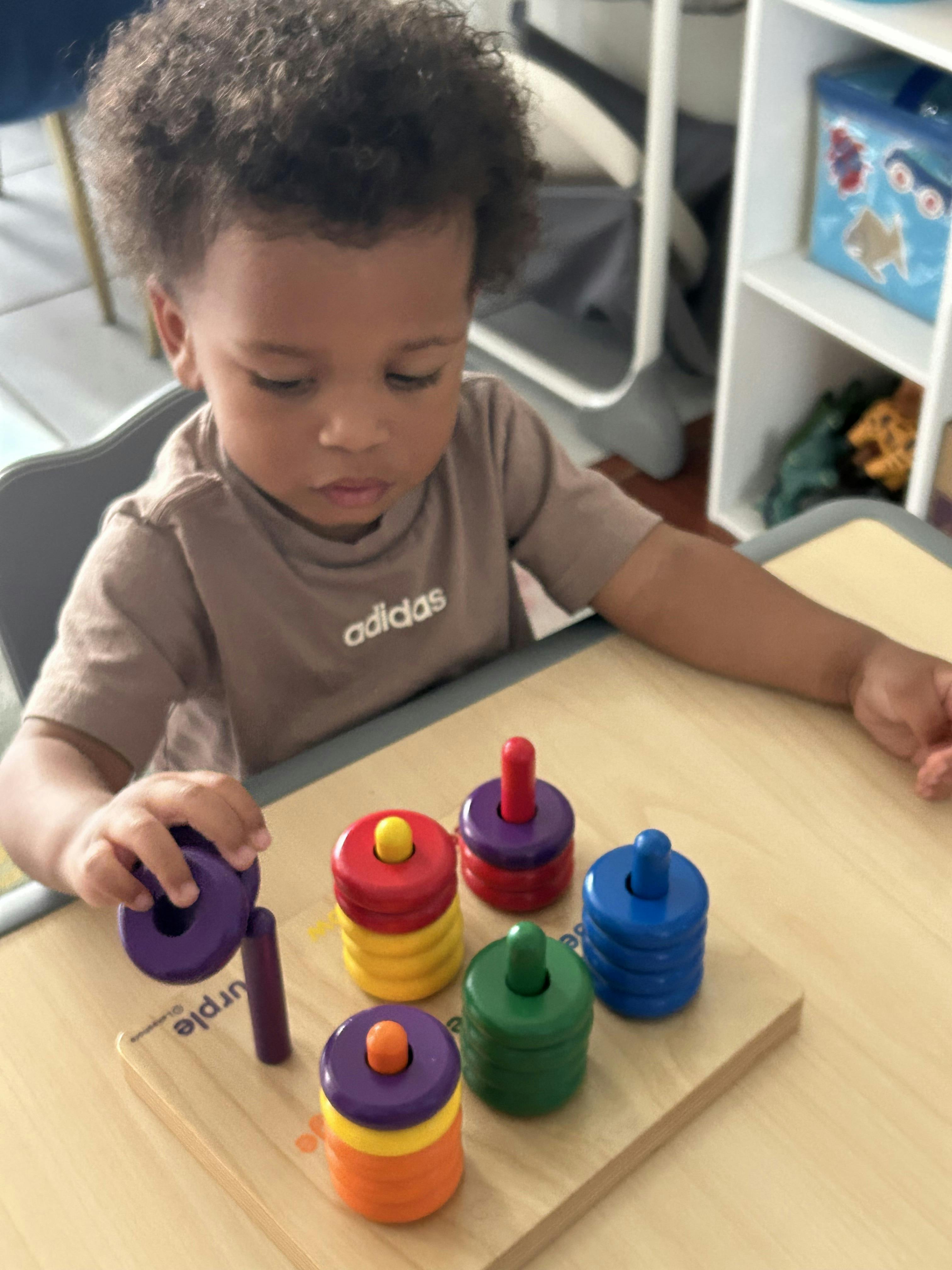 Child playing with a colorful stacking ring toy at a table