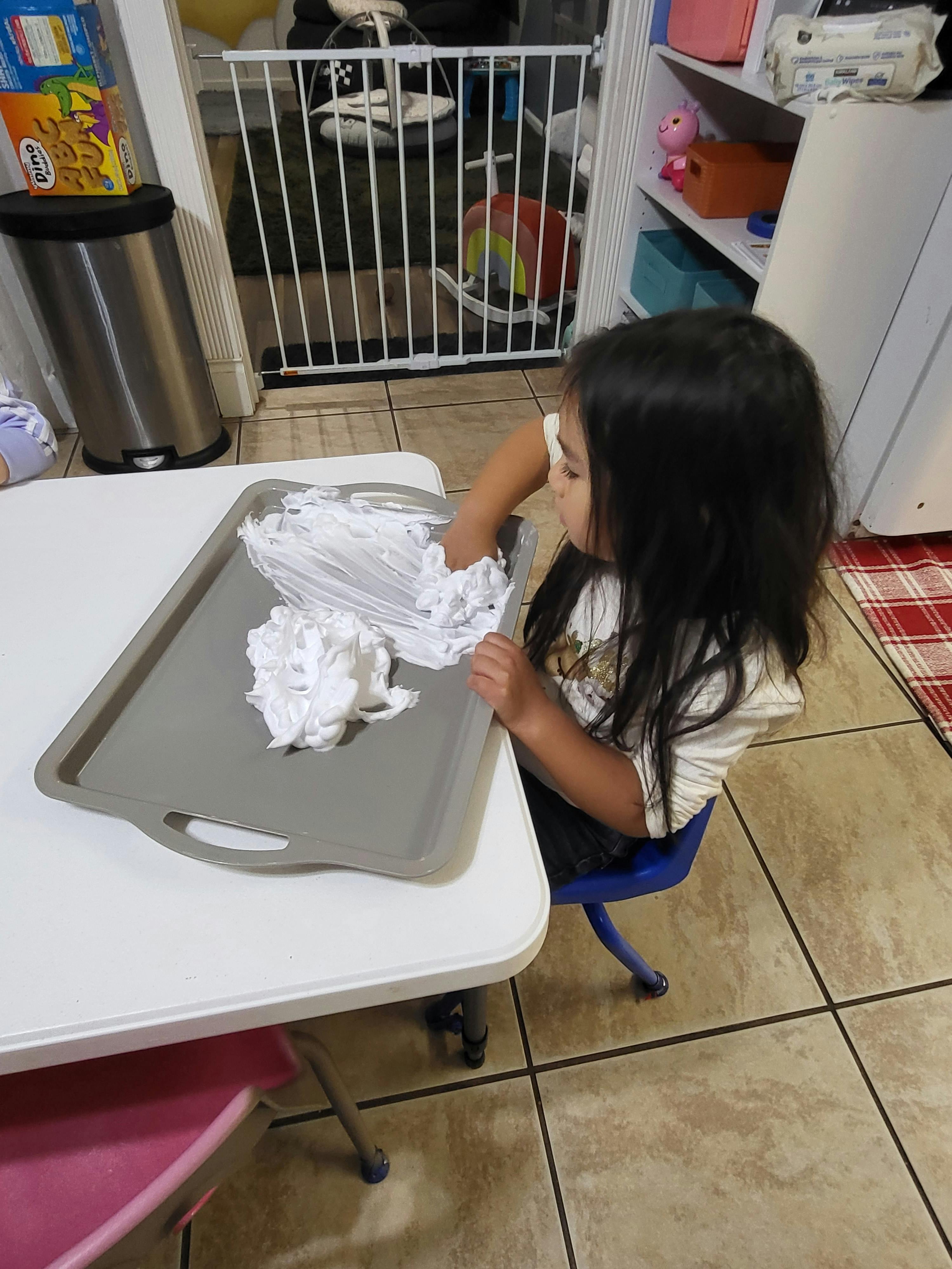 Child playing with shaving cream on a tray at a table