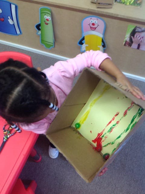 Child holding a cardboard box with paint and marbles inside