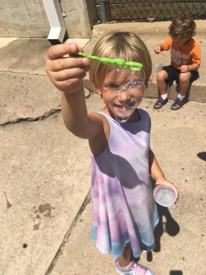 Child holding a bubble wand with bubbles on their face