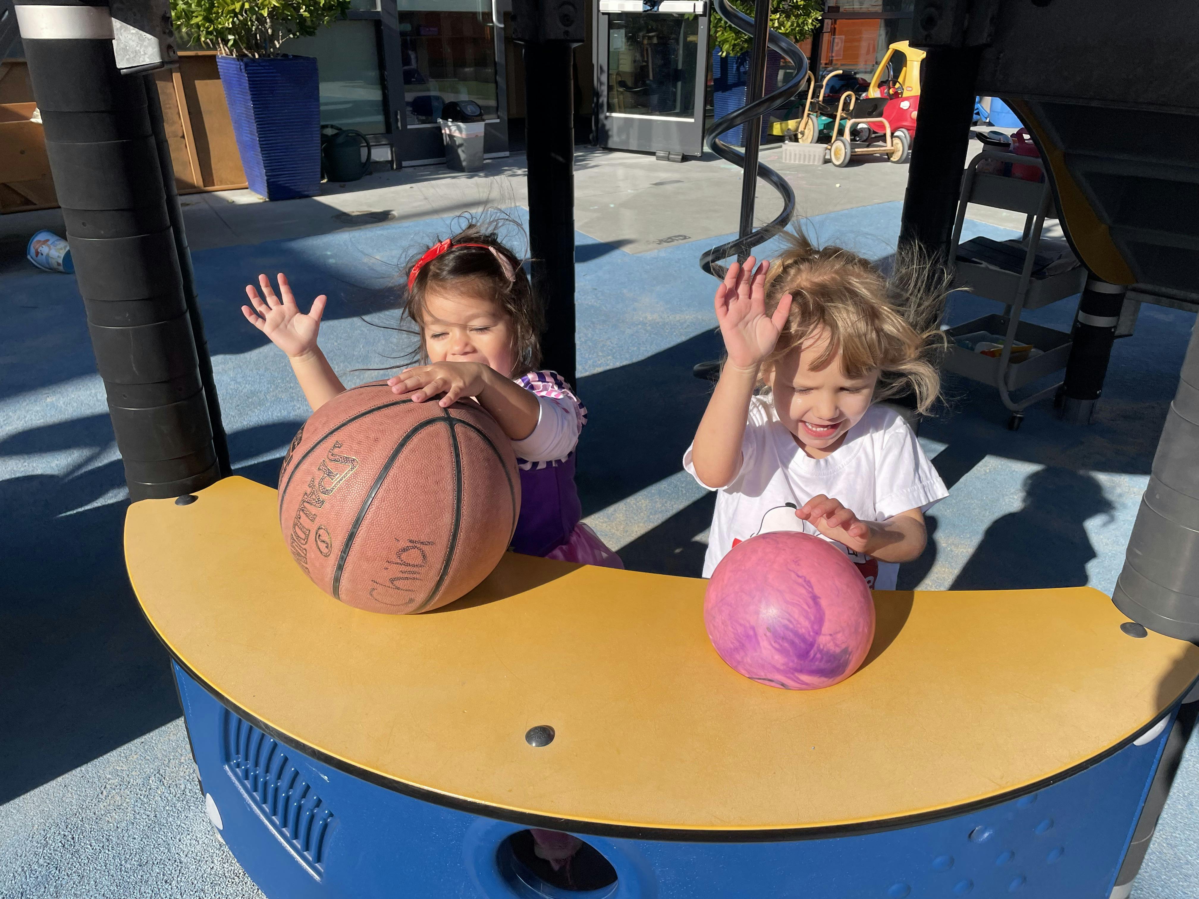 Two children playing with balls on a playground structure