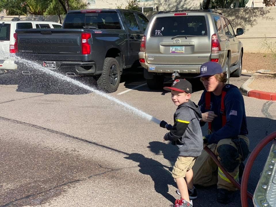 Person in uniform helping a child spray water from a hose