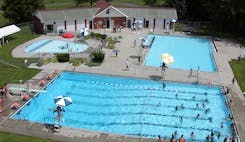 People swimming in multiple outdoor pools with a building in the background