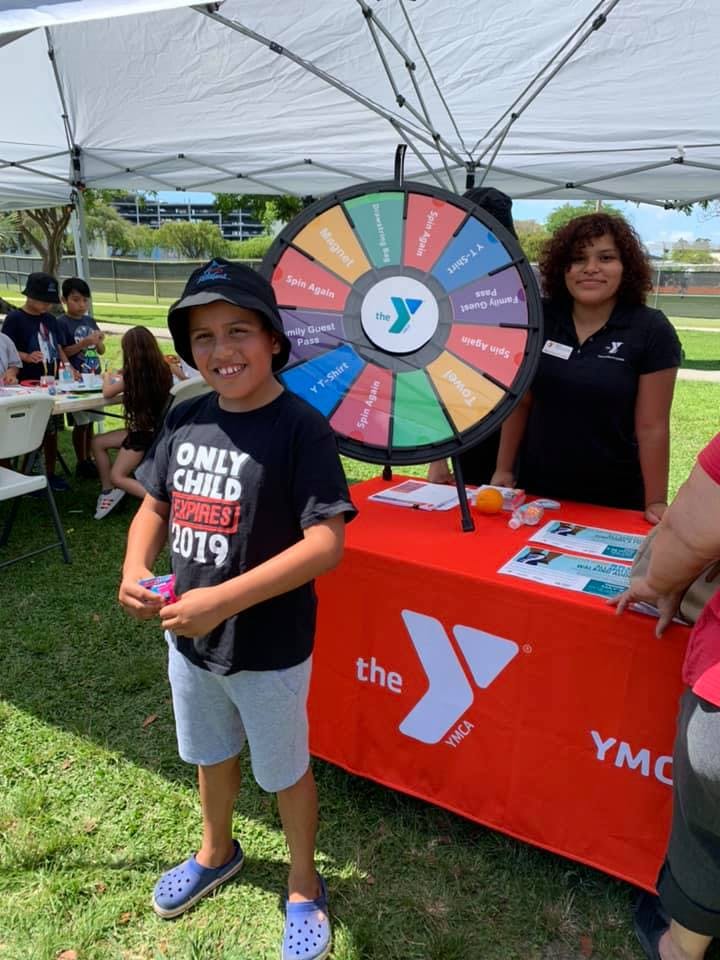 Child in a hat standing next to a prize wheel and a person behind a table