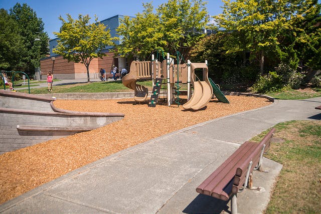 Playground with slides and climbing structure next to a concrete path and bench
