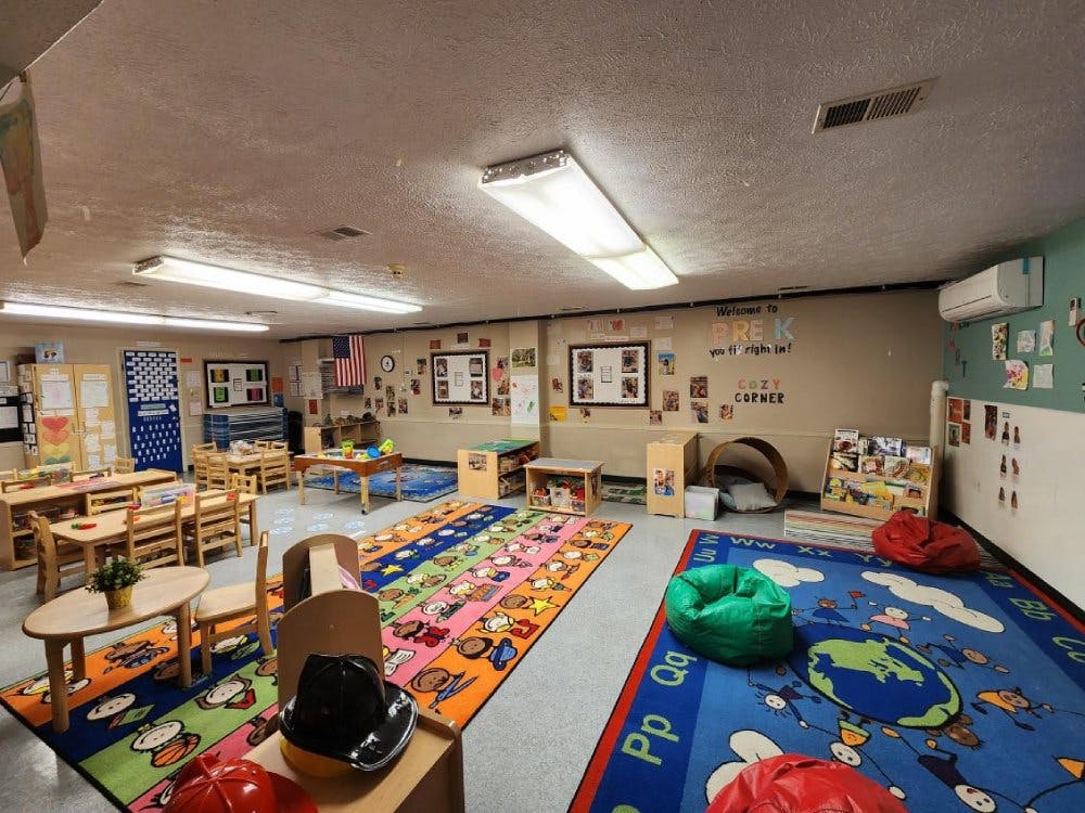 A colorful empty preschool classroom with tables, chairs, rugs, and a cozy corner