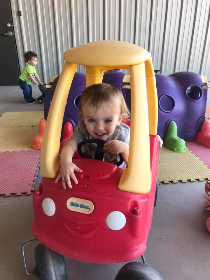 Child in a red toy car, another child in background