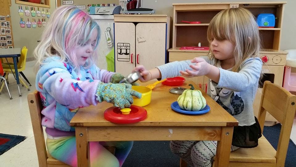 Two children playing with toy kitchenware at a table in a classroom