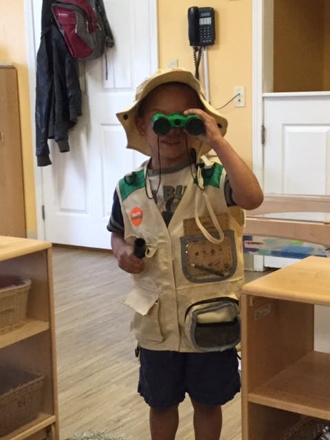 Child in a safari hat and vest looking through green binoculars