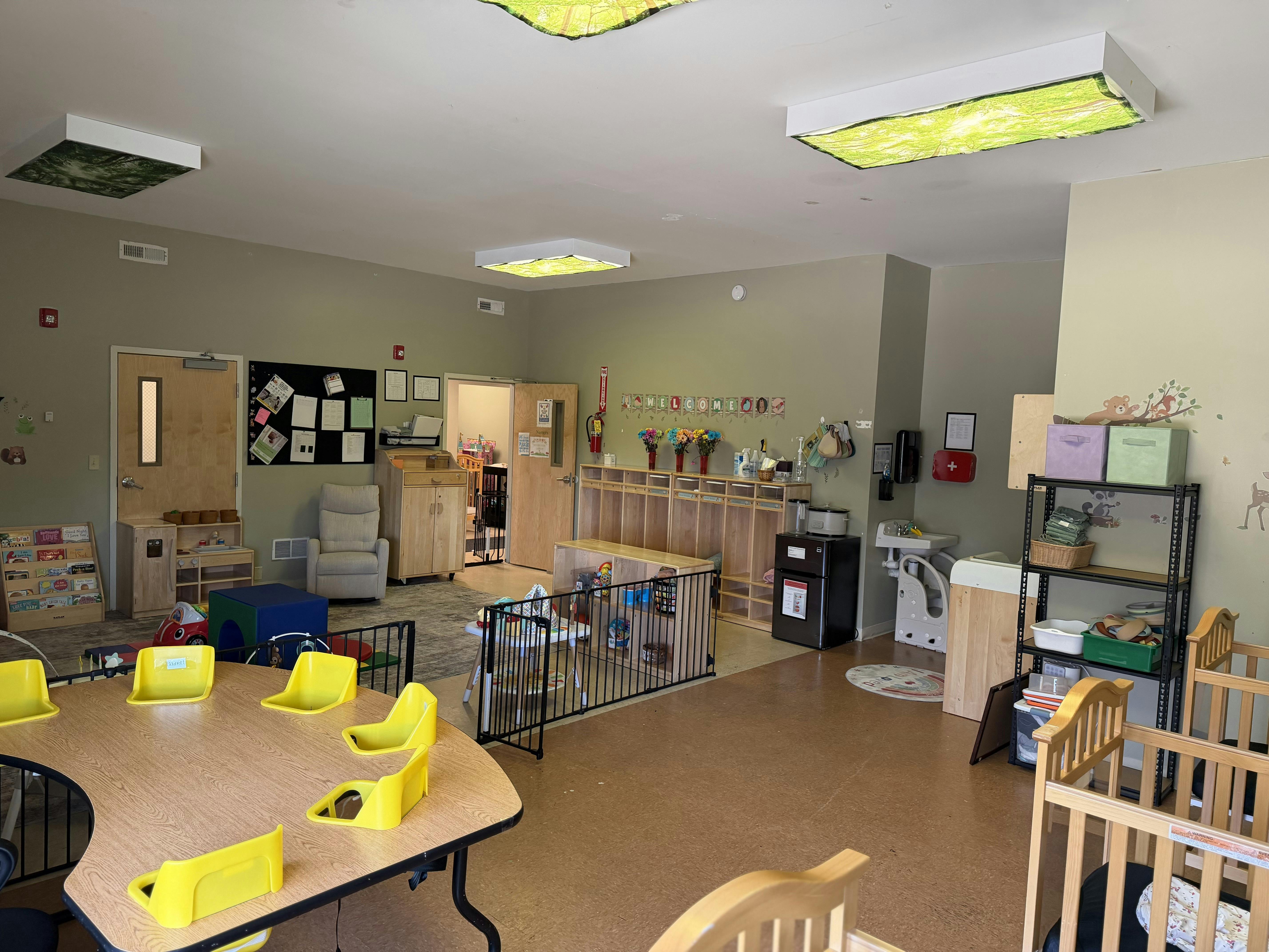 A childcare classroom with tables, chairs, cribs, play areas, and storage cubbies