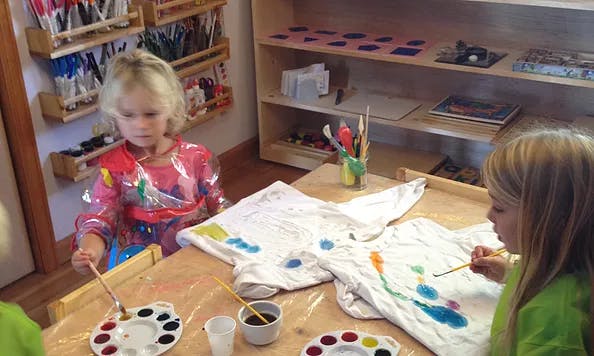Two children painting shirts at a table