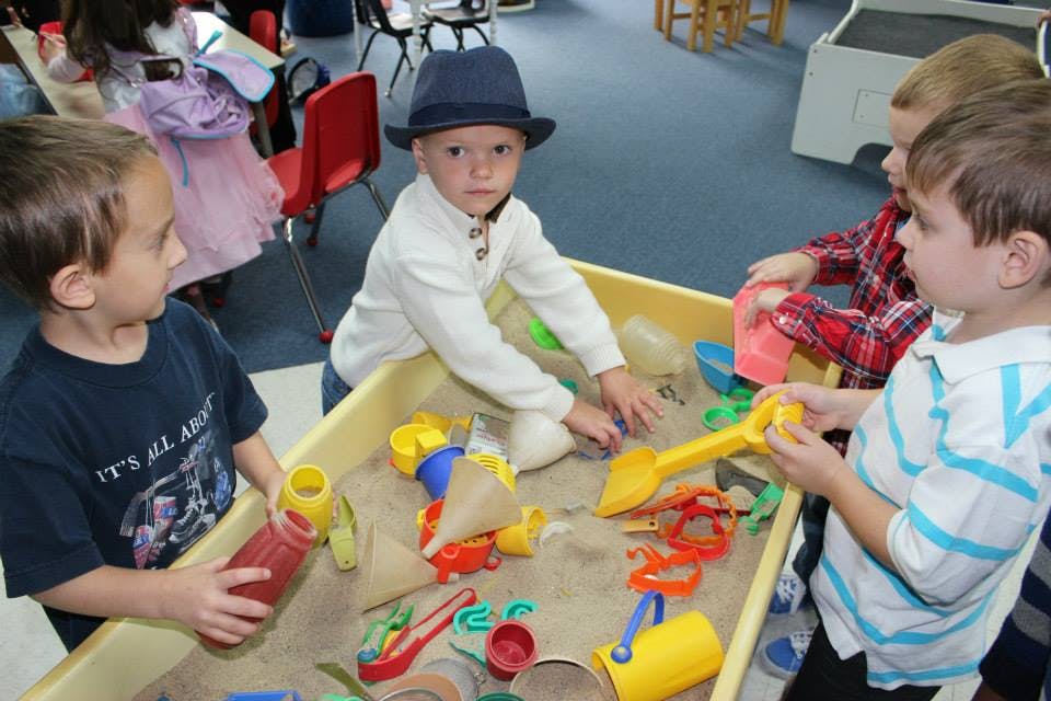 Three children playing in a sand table with toys