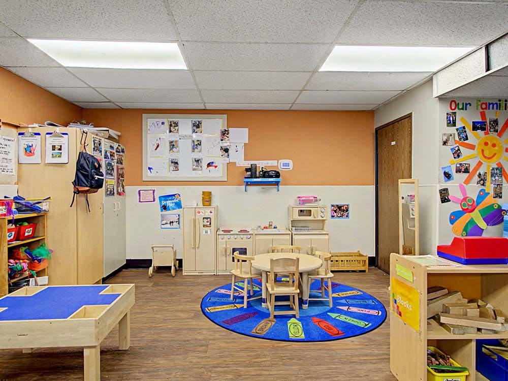 Empty classroom with small tables and chairs, play kitchen, and storage shelves
