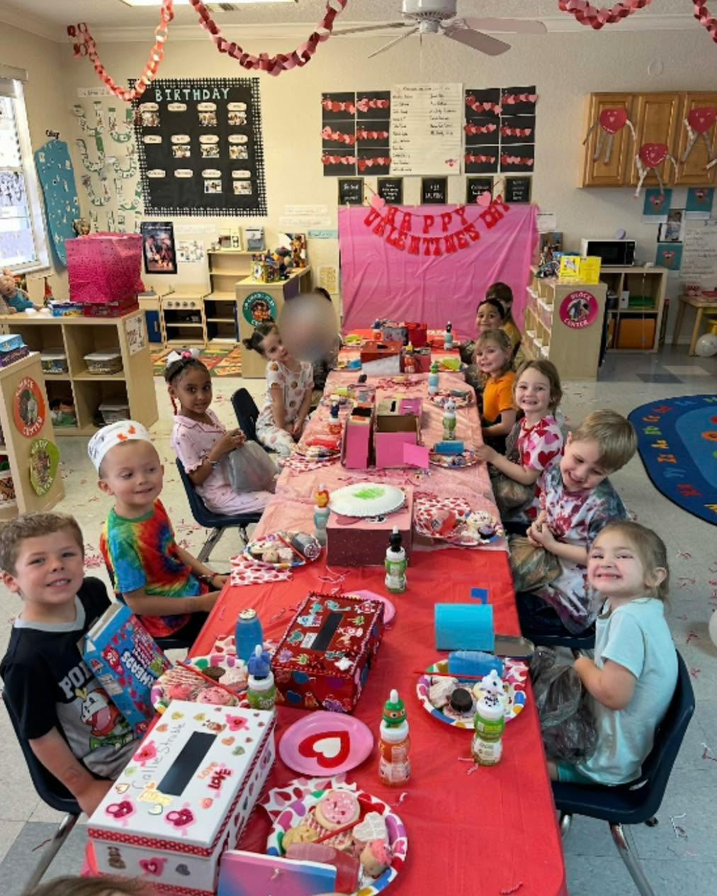 Group of children seated around a table for a Valentine Day party in a classroom