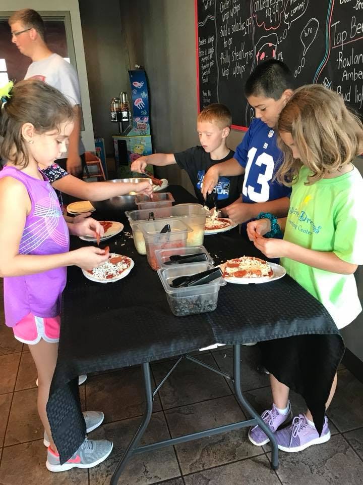 Children making individual pizzas at a table