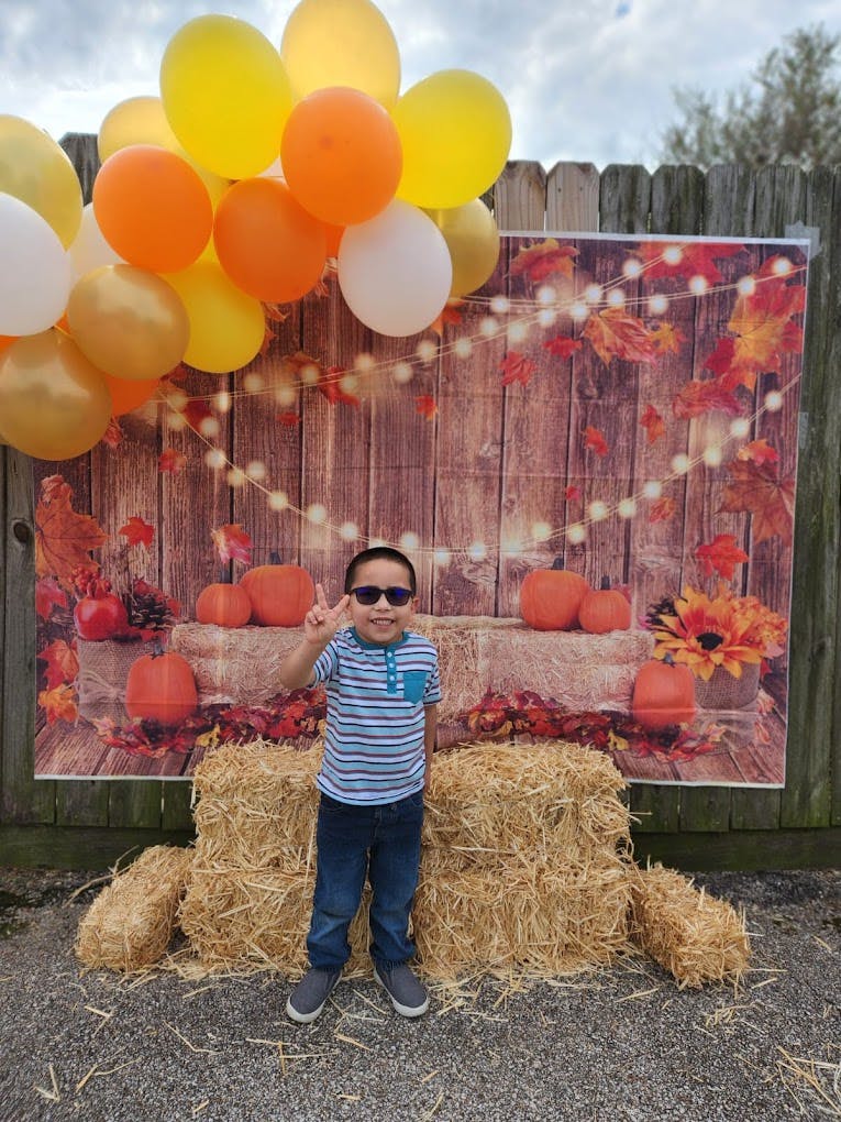 Child in sunglasses making a peace sign in front of a fall-themed backdrop