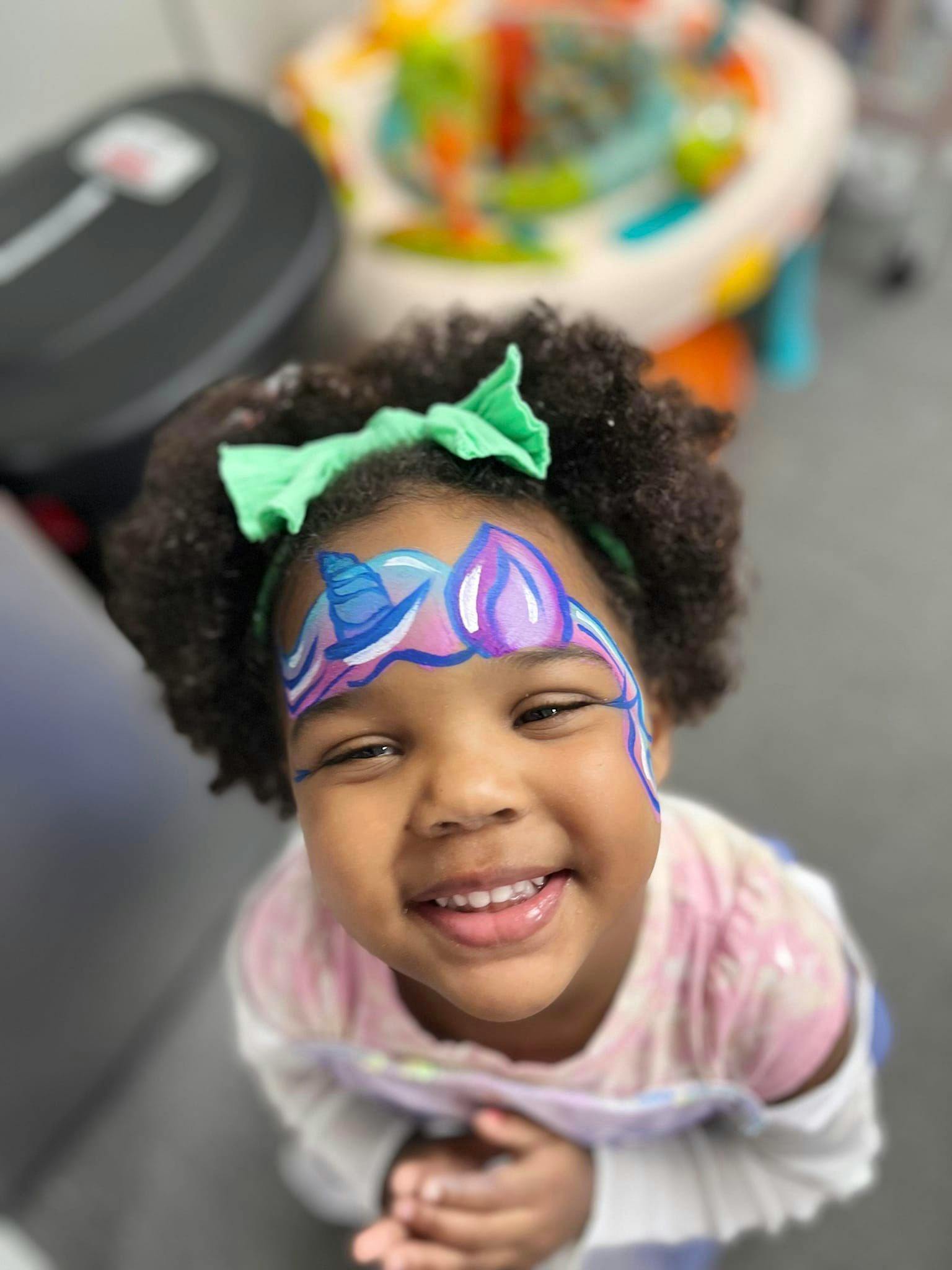 Child with face paint and a green bow in their hair