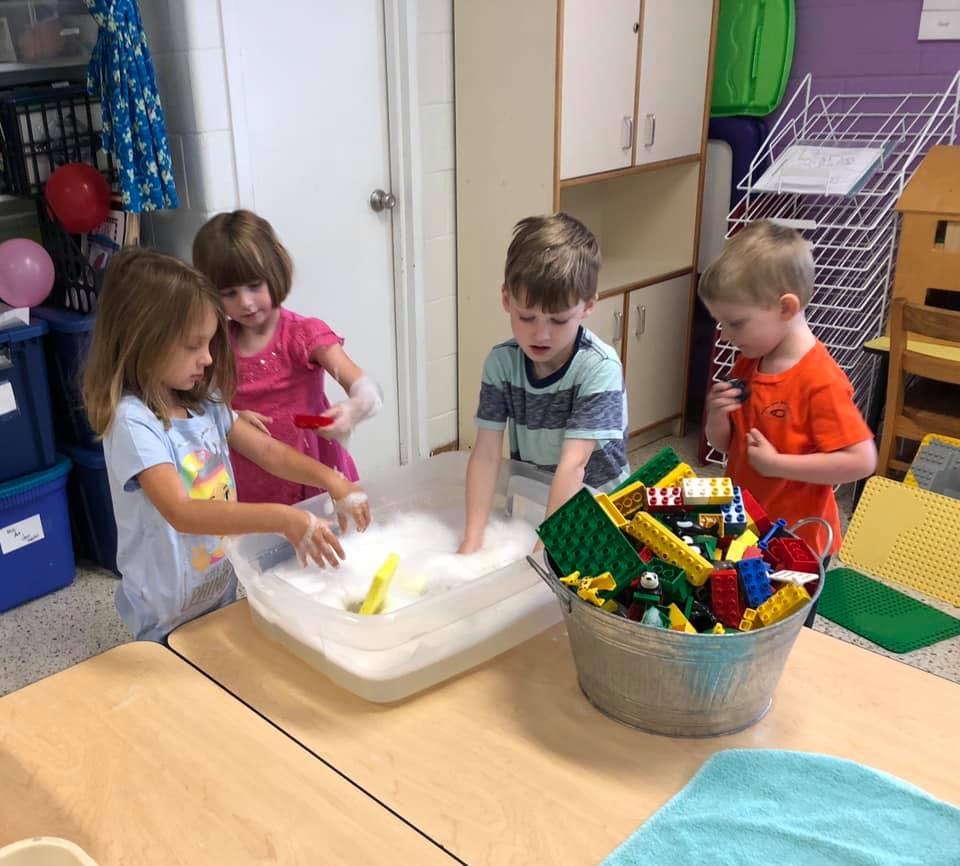 Four children playing with soapy water and toys in a classroom