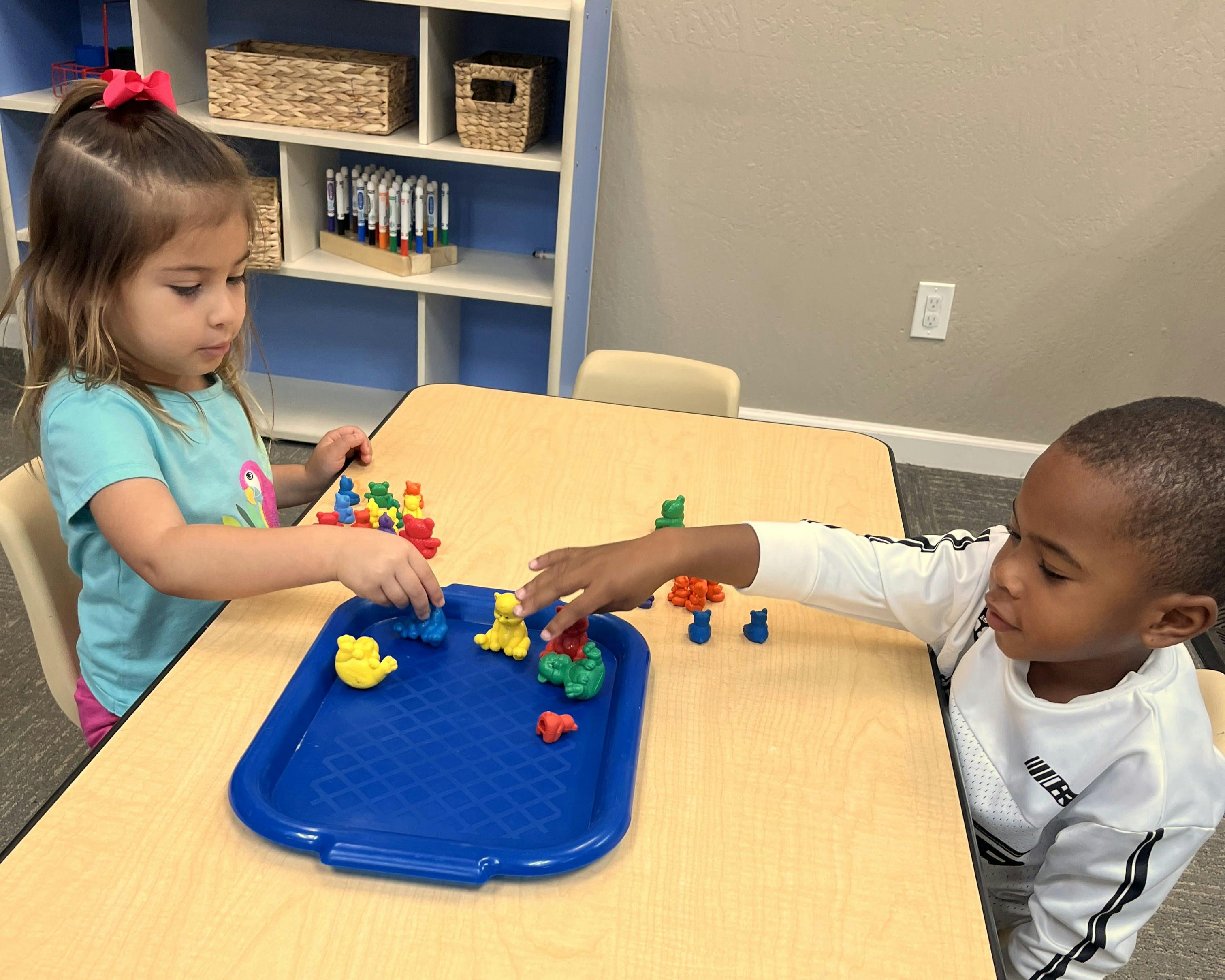 Two children playing with small colorful plastic bear figurines at a table