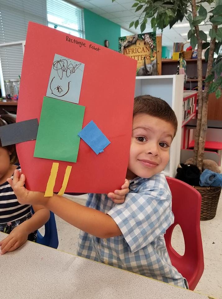 Child holding up a red paper craft with smaller colored paper shapes