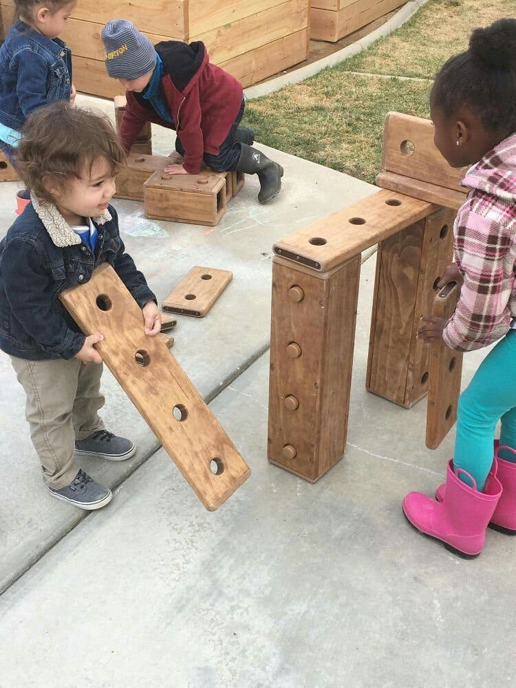 Children playing with large wooden building blocks outdoors