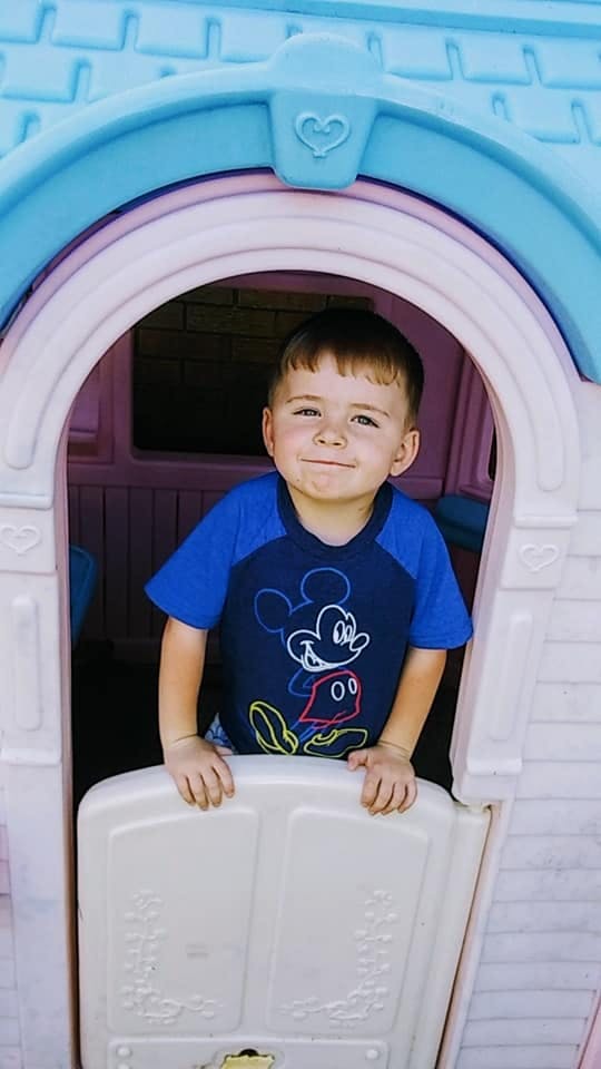 Child in a blue shirt with Mickey Mouse design looking out of a playhouse window