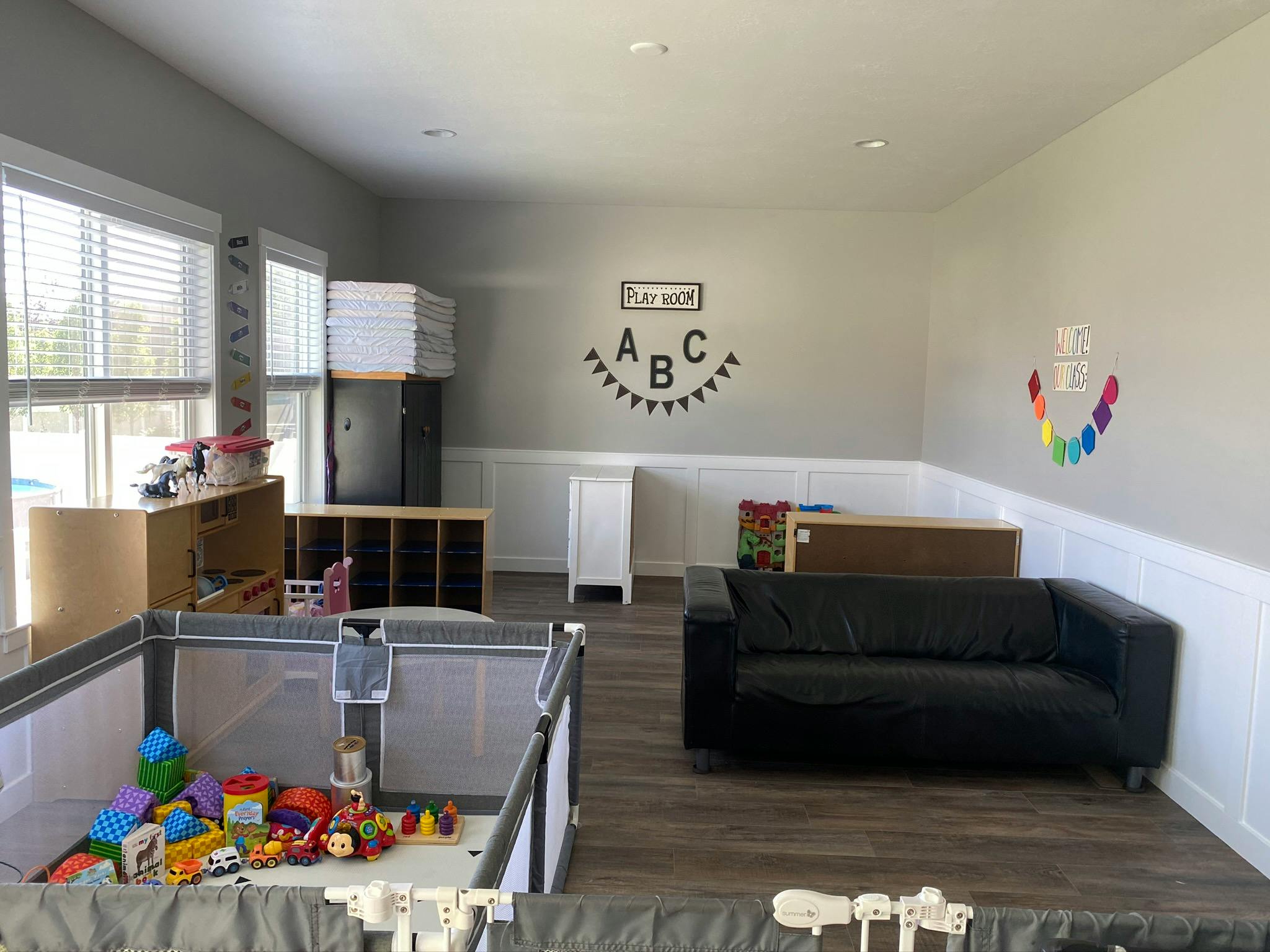Playroom with a playpen full of toys, a black sofa, and ABC wall decor
