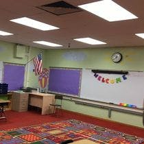 Classroom with a whiteboard displaying "WELCOME" and a colorful rug
