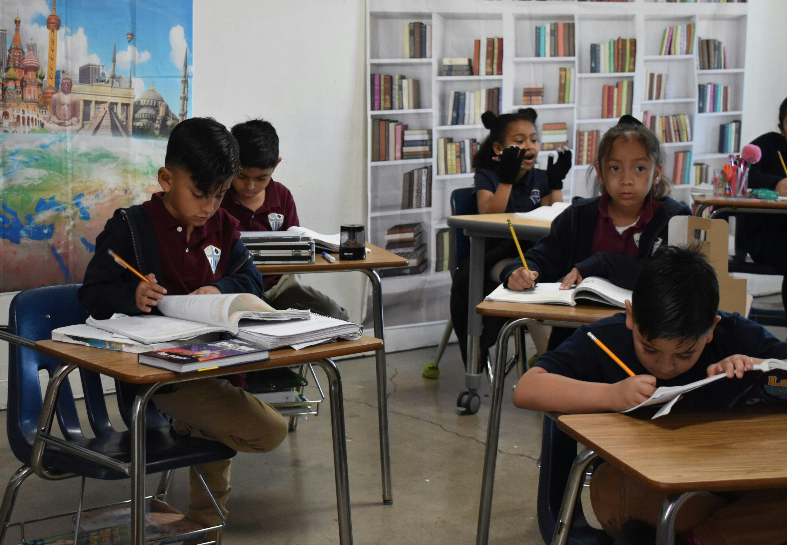 Children writing and looking at books at desks in a classroom