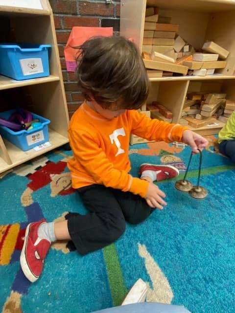 Child playing with cymbals on a colorful rug in a classroom