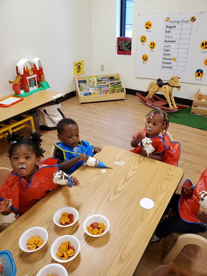 Three children eating ice cream at a table in a classroom