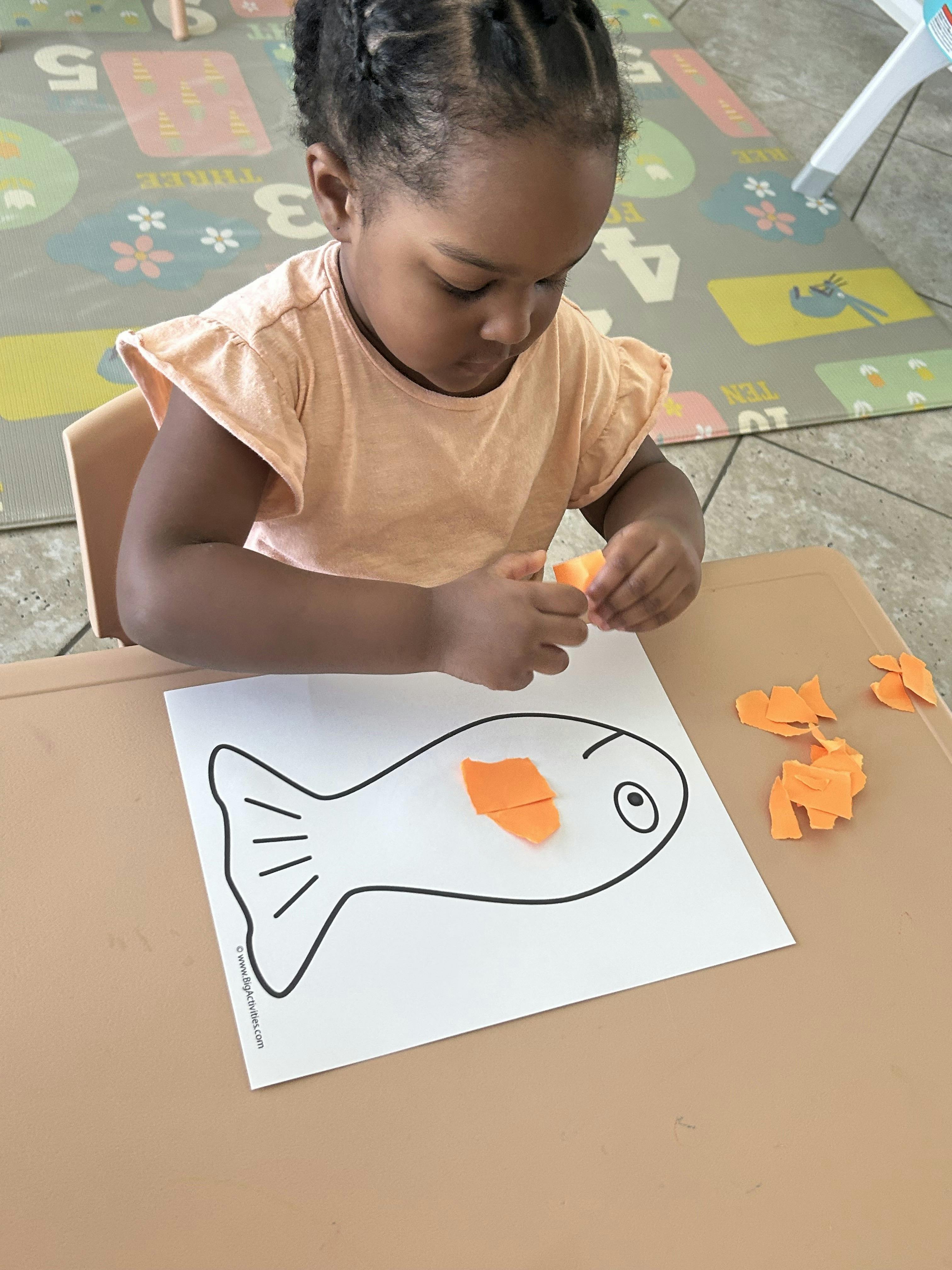 Child placing orange paper pieces onto a fish outline