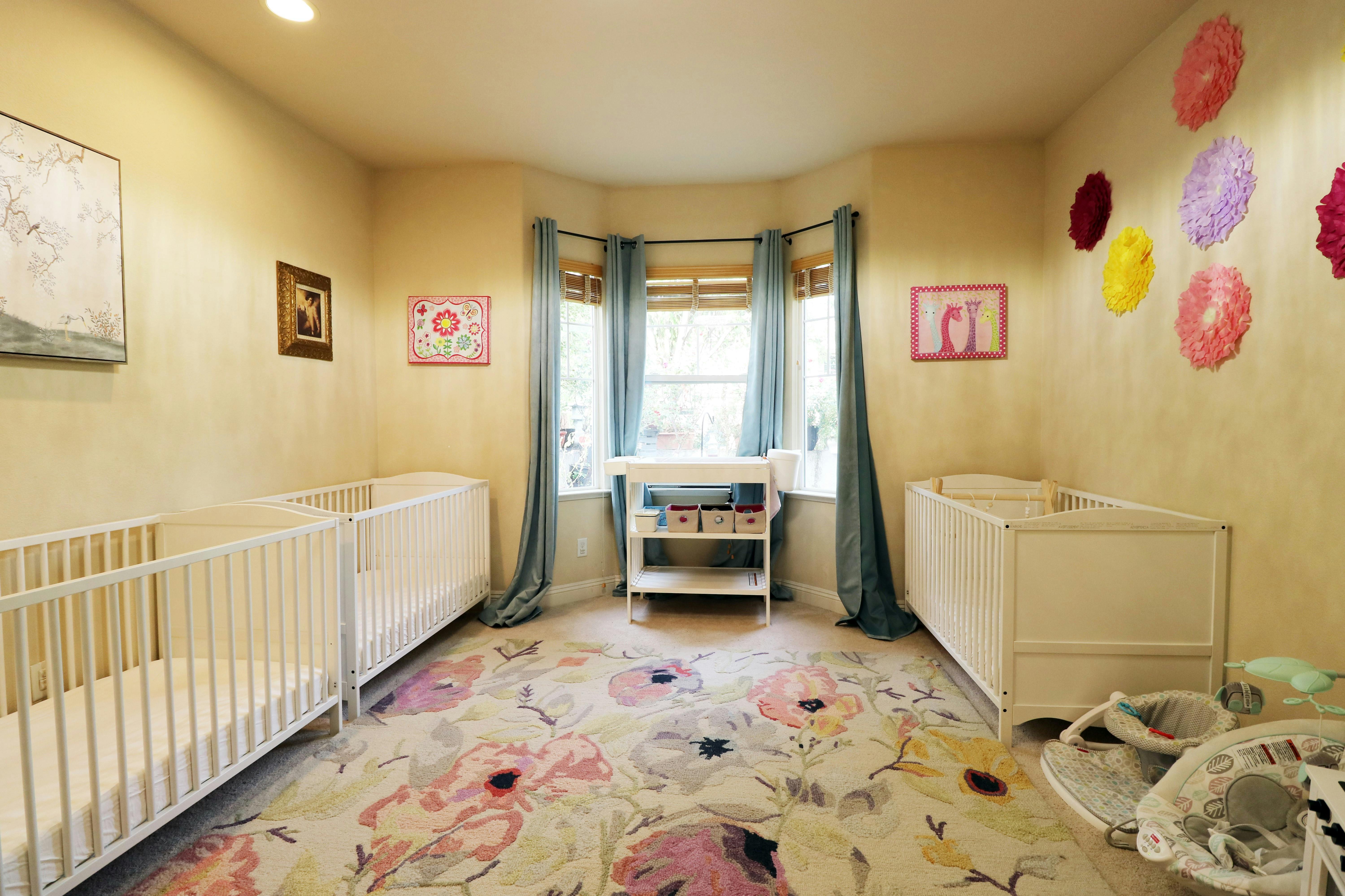 Nursery room with three cribs, a changing table, and a floral rug