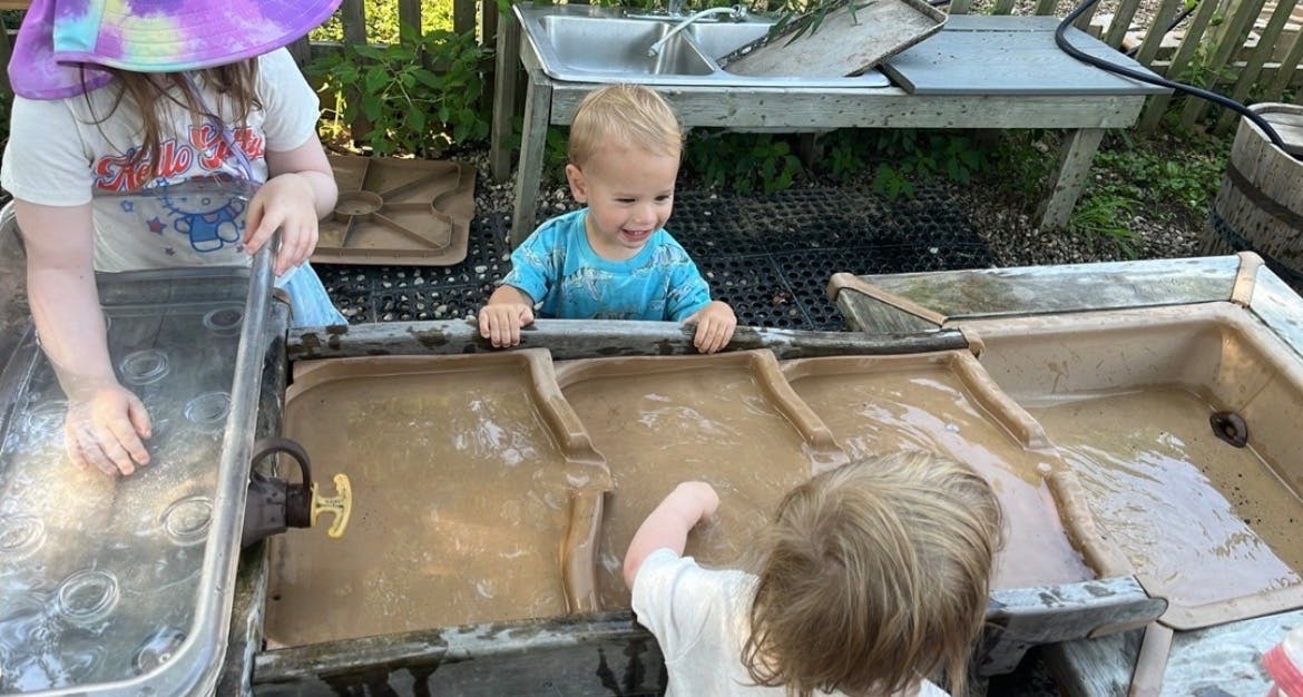 Three children playing with water in a sensory table outdoors
