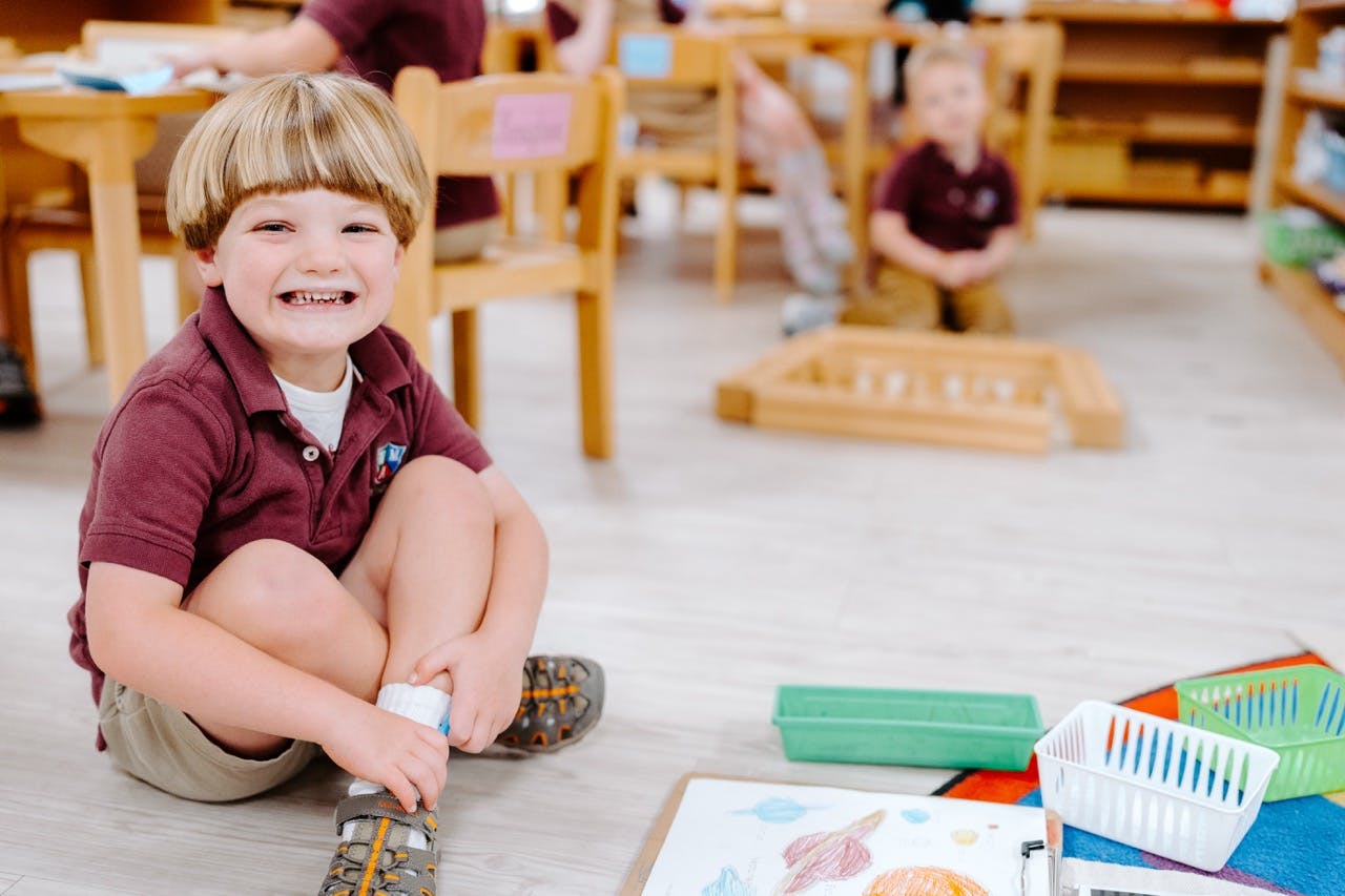 Child sitting on the floor in a classroom, smiling