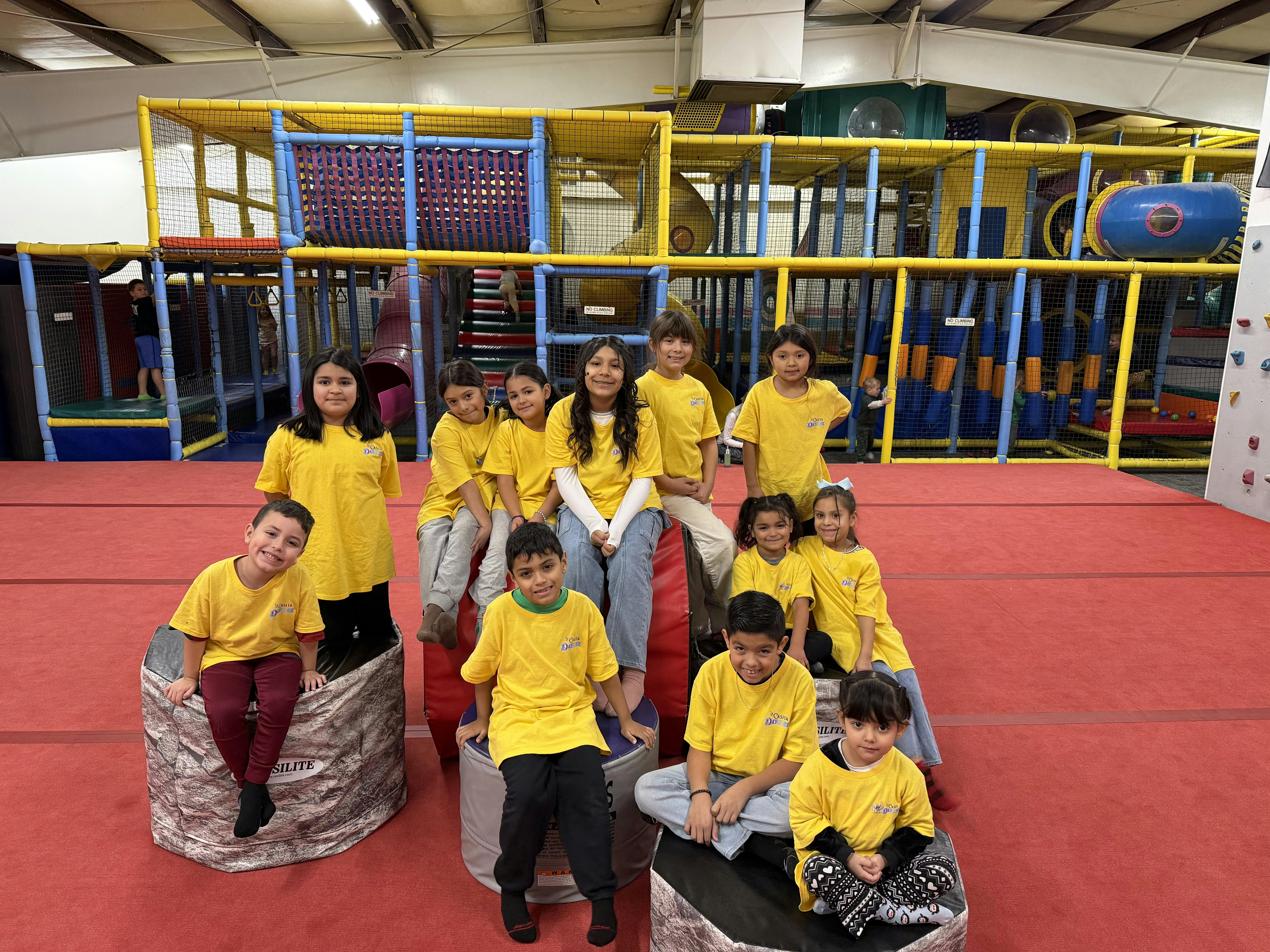 Group of children and teens posing in yellow shirts at an indoor playground