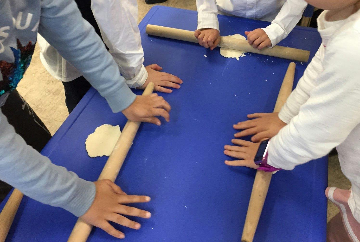 Children rolling dough with rolling pins on a blue table