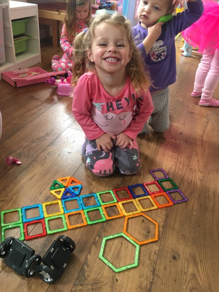 Child kneeling on floor with colorful magnetic tiles and toy cars