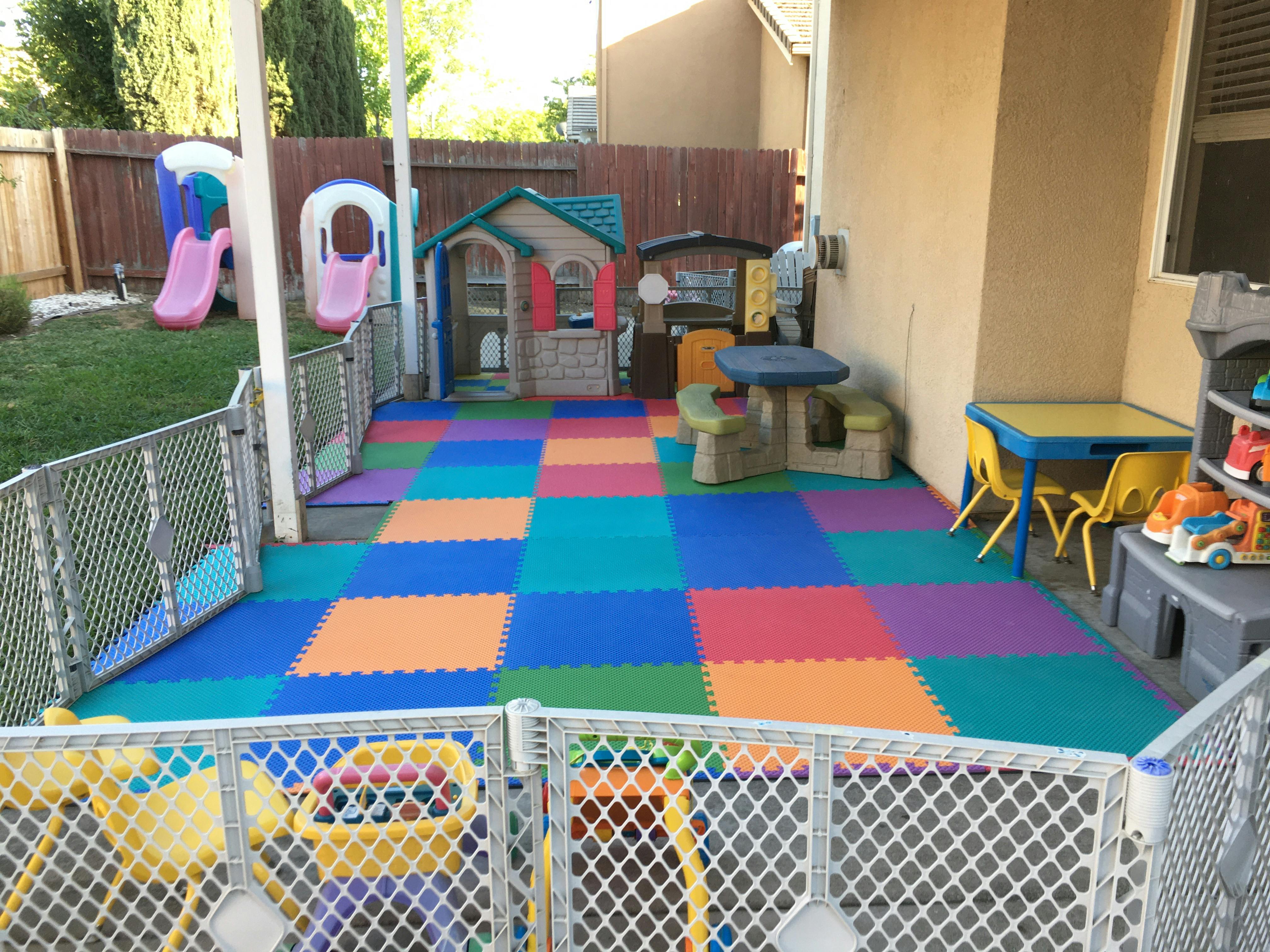 Outdoor play area with colorful foam mats, playhouses, and small tables