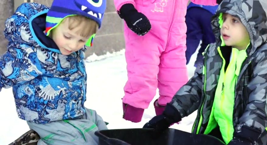 Two children in winter clothing playing in snow