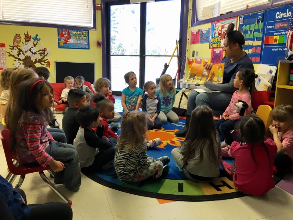 Person reading a book to a group of children in a classroom