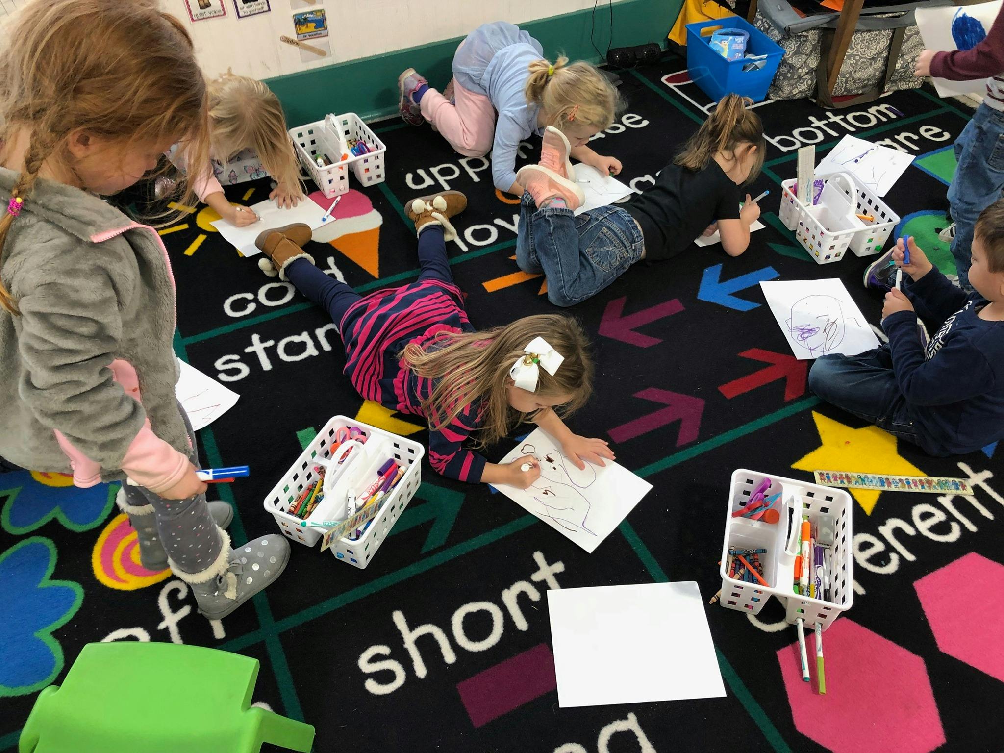Children drawing and writing on a classroom rug