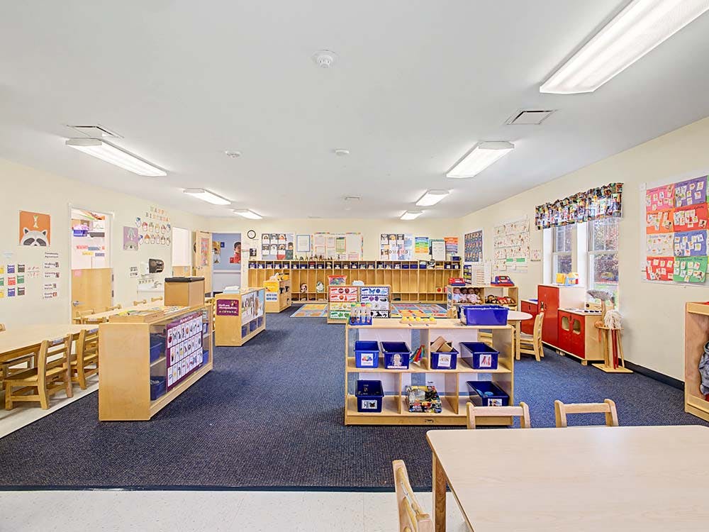 Empty classroom with small tables and chairs, shelves with toys
