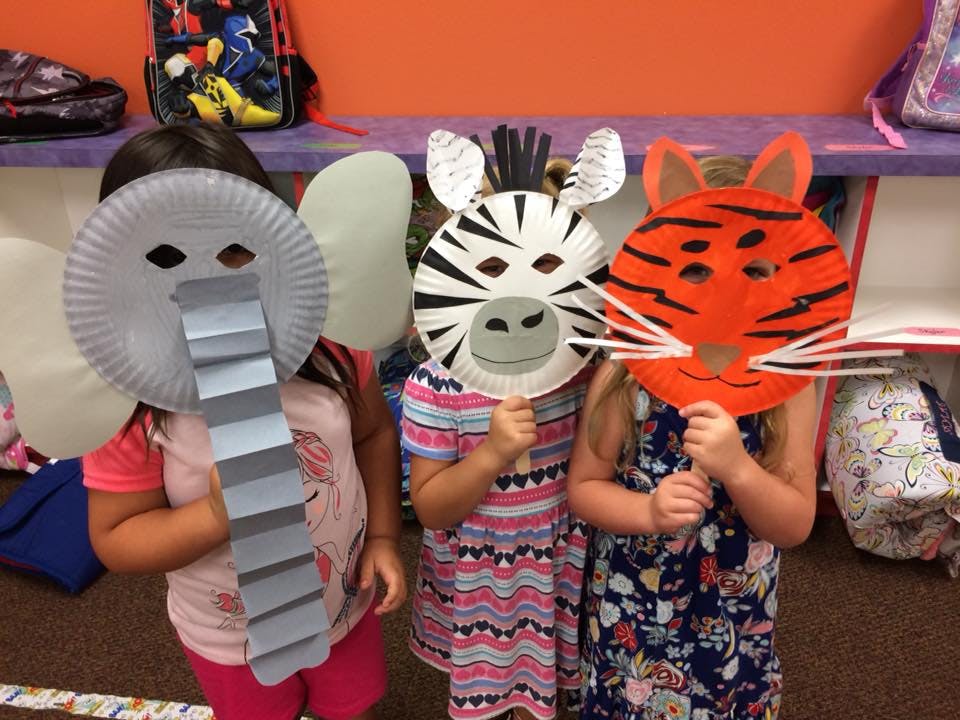 Three children holding up paper plate animal masks