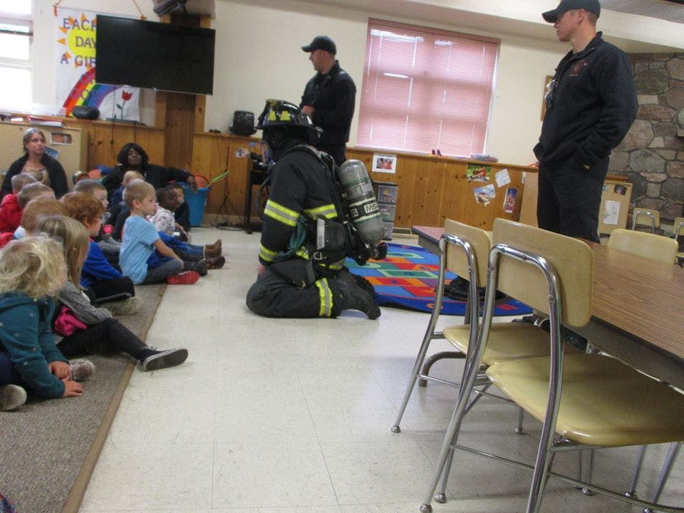 Firefighter in full gear kneeling in front of children sitting on floor