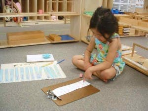 Child sitting on floor pointing at paper on a clipboard
