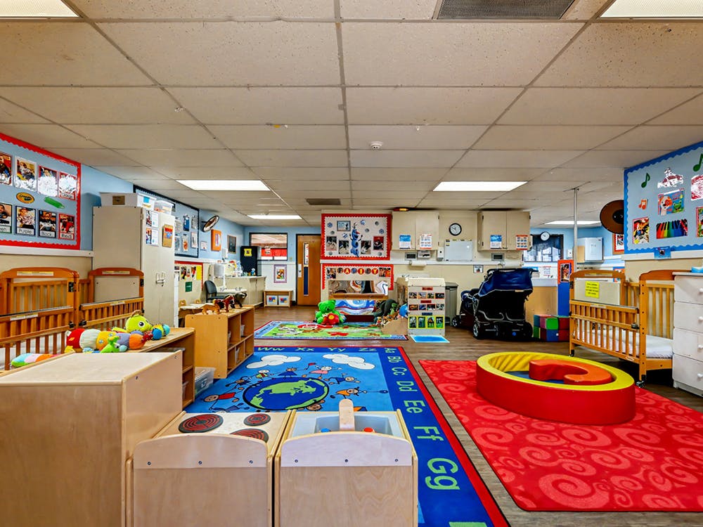 A colorful childcare classroom with cribs, play mats, and learning charts