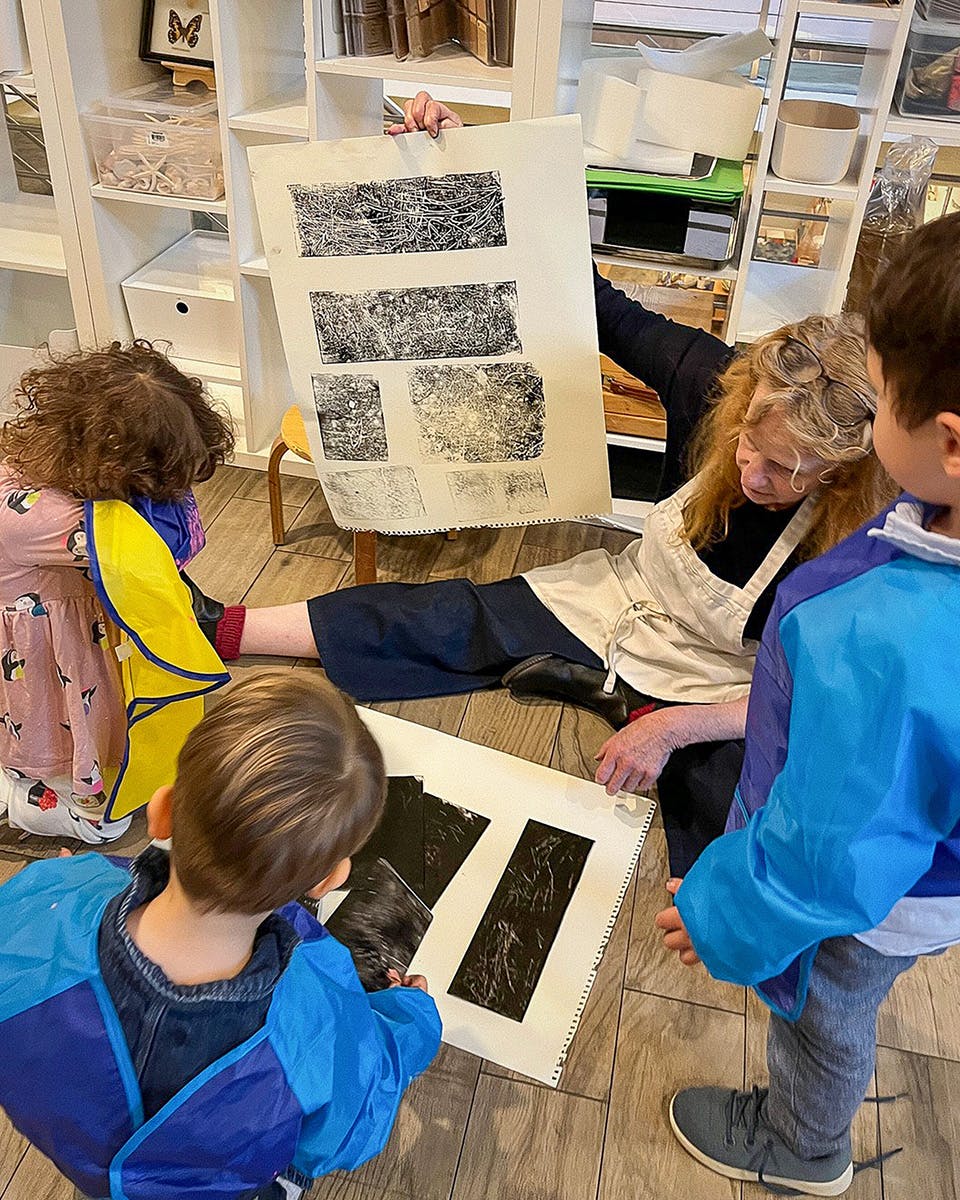 Adult and three children looking at art prints on paper