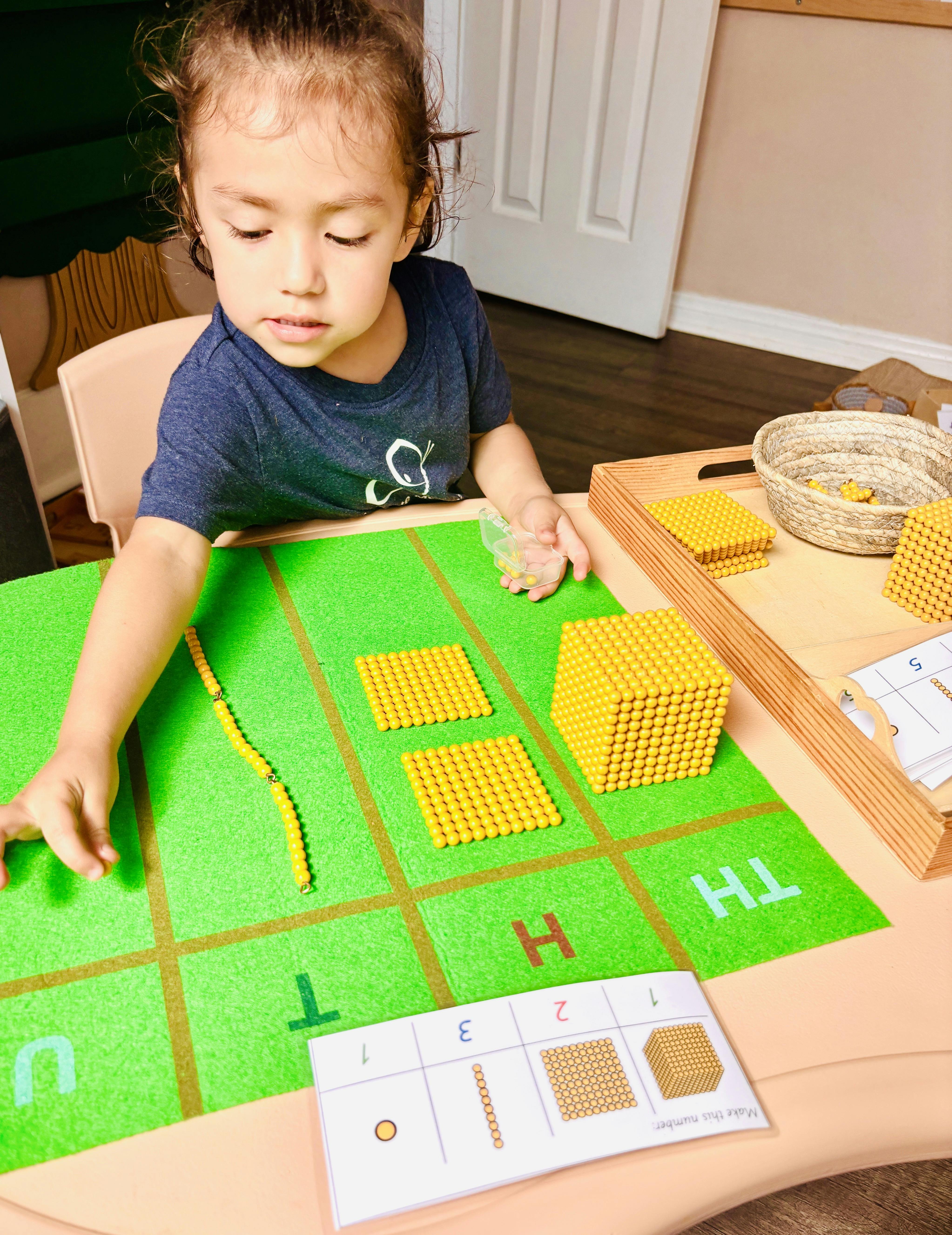 Child learning math using Montessori beads and a green mat with gold felt mat