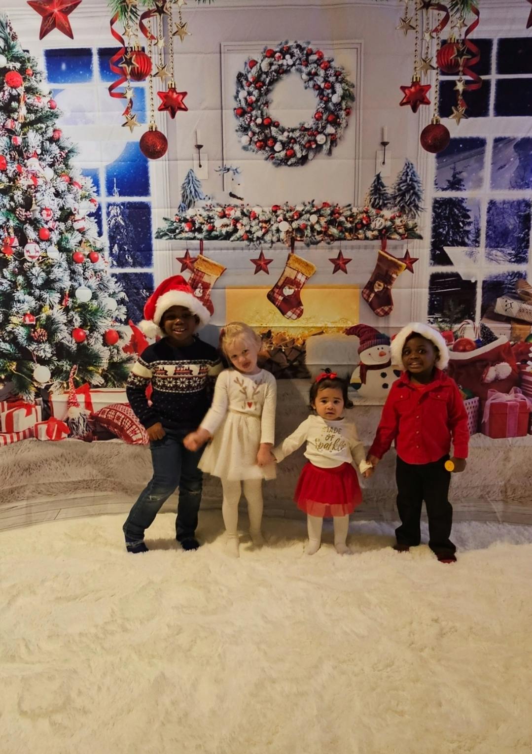 Four children in holiday attire posing against a Christmas themed backdrop